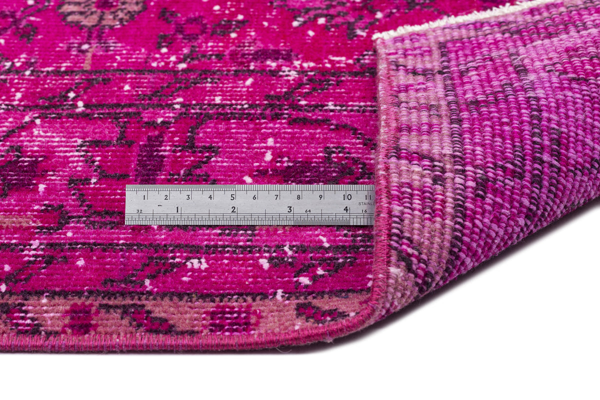 Magenta distressed rug with a black floral medallion pattern, shown with a metal ruler for scale.