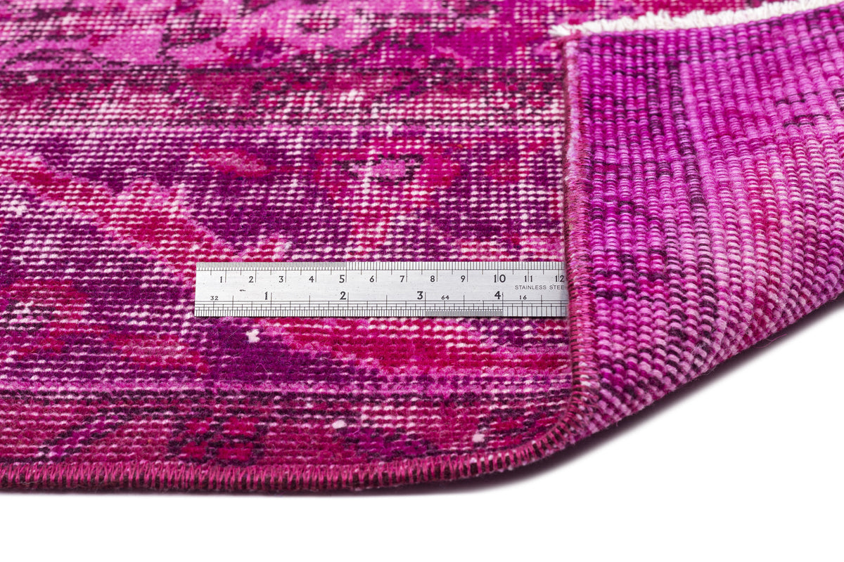 Magenta and purple distressed floral rug with a folded corner and a stainless steel ruler for scale.