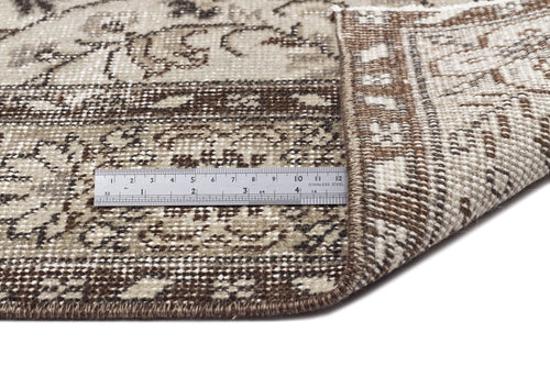 Load image 1 in gallery view. A close-up shows the corner of the Sigima - Vintage Floral Rug (5'4 x 9'1) flipped over to reveal its back, with a metal ruler displaying cm and inch markings for scale. The rug features brown, beige, and cream vintage-inspired designs.