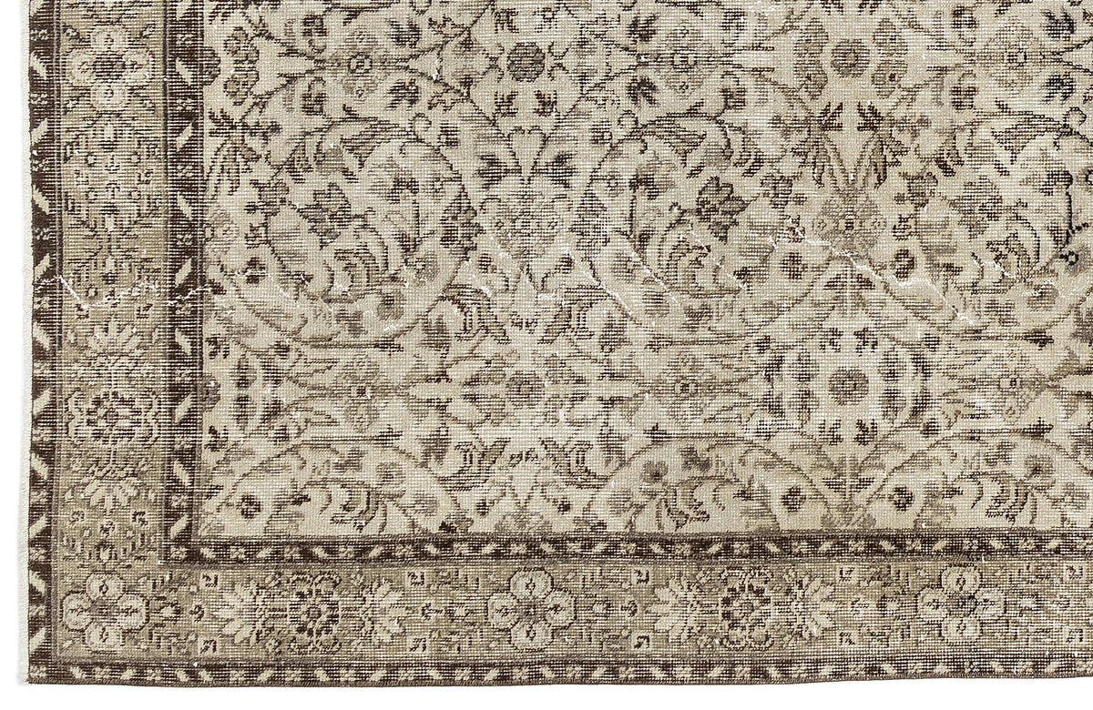 A close-up of the Sigima - Vintage Floral Rug (5'4" x 9'1") shows its beige and brown tones, intricate floral and vine patterns, and decorative border that highlight the artisanal detail of this traditional hand-woven piece.