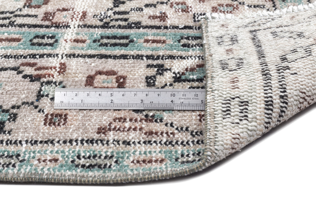 Beige, teal, and brown distressed traditional rug with a metal ruler showing pile height on a white background.