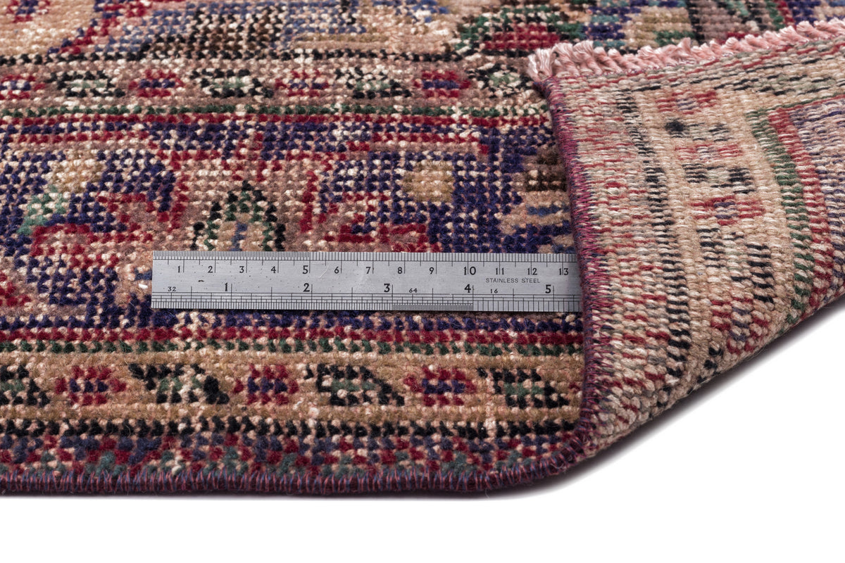 Multi-colored traditional patterned rug with a folded corner and a stainless steel ruler for scale.