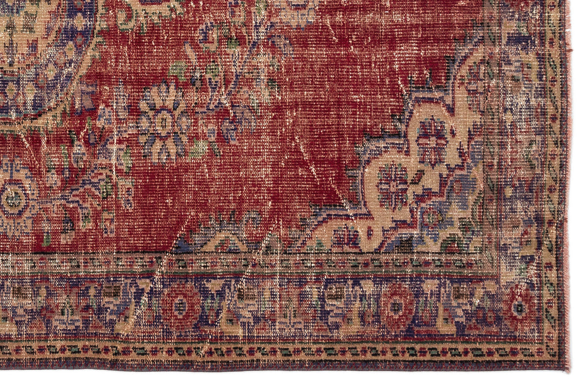 Distressed red rug with a beige and blue floral medallion pattern and a detailed geometric border.