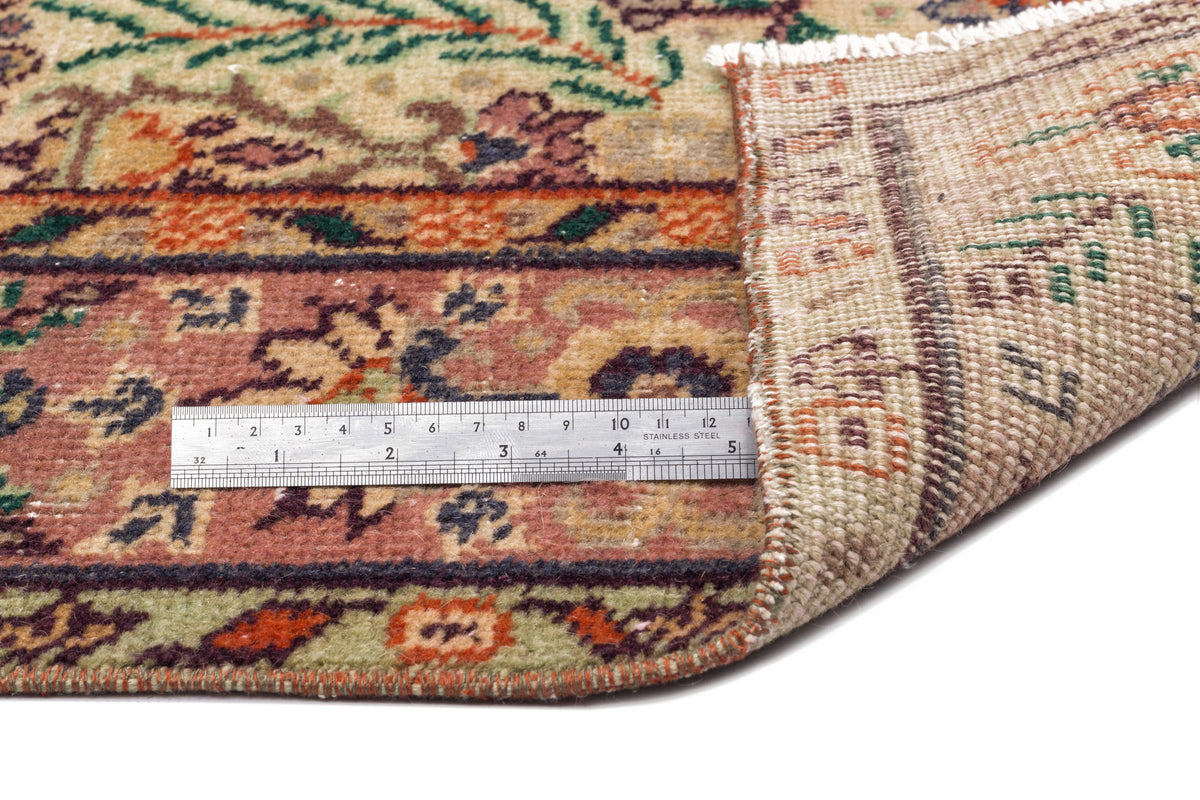Multi-colored floral patterned rug with a folded corner and a metal ruler for scale on a white background.