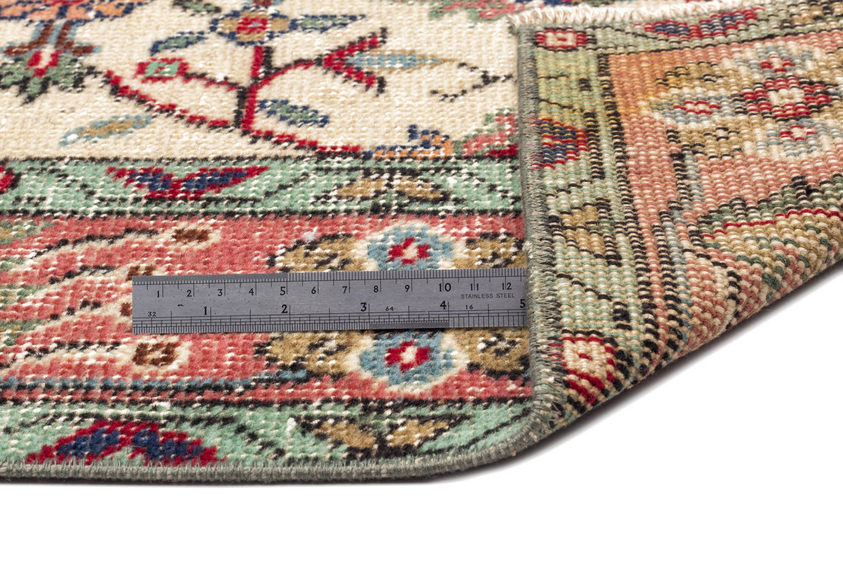 Multi-colored traditional rug with floral motifs and a geometric border, shown folded with a metal ruler for scale.