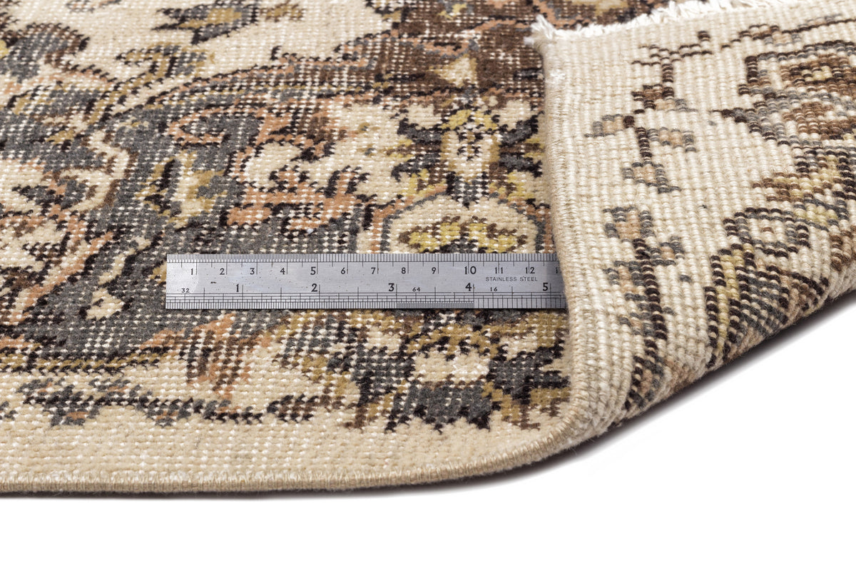 Beige, brown, and charcoal traditional medallion rug with a folded corner and a metal ruler for scale.
