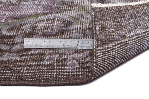 Load image 1 in gallery view. Brown and purple distressed floral rug with a folded corner and a metal ruler for scale on a white background.