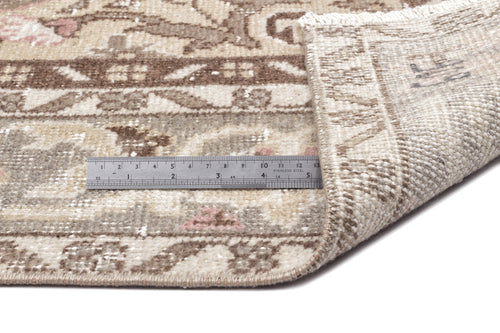 Load image 1 in gallery view. Beige and brown vintage-style rug with floral motifs and a folded corner, shown with a metal ruler for scale.