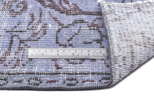 Load image 1 in gallery view. Periwinkle and charcoal distressed floral rug with a folded corner and a metal ruler for scale.