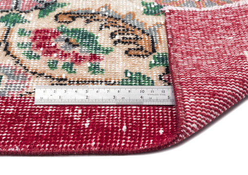 Load image 1 in gallery view. Red and beige floral medallion rug with a folded corner revealing the underside, shown with a metal ruler for scale.