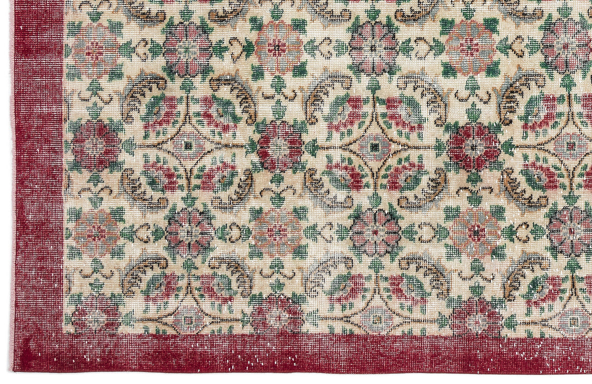 Beige rug with a red border and a repeating floral medallion pattern in red, green, and muted blue.
