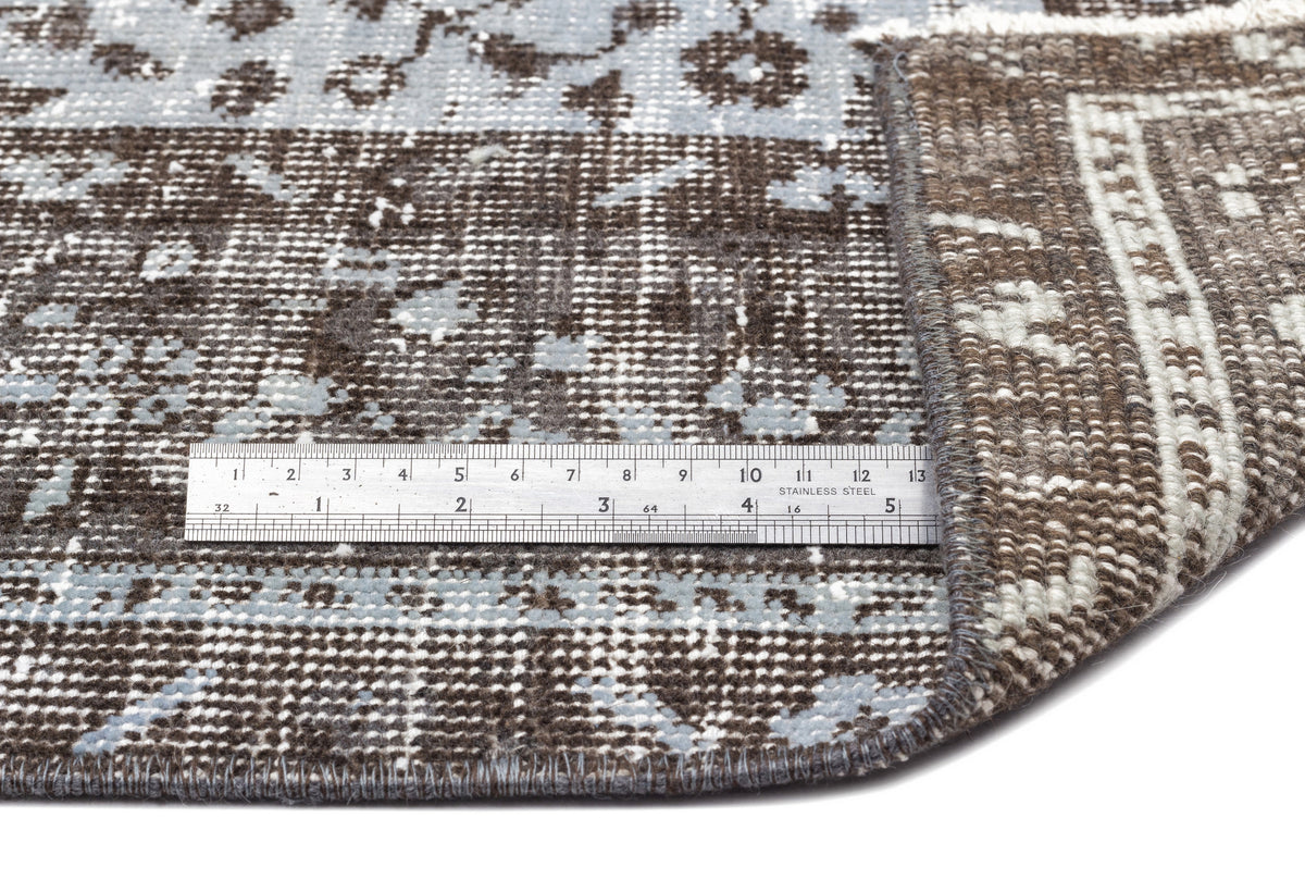 Brown and light blue distressed traditional rug with a folded corner and a metal ruler for scale.