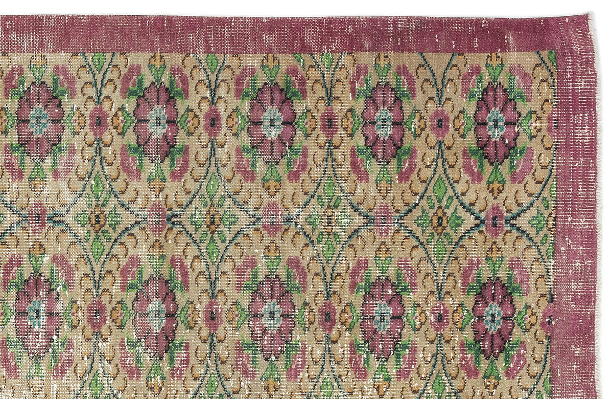 Distressed beige rug with a magenta border and a repeating floral medallion pattern in magenta, green, and teal.