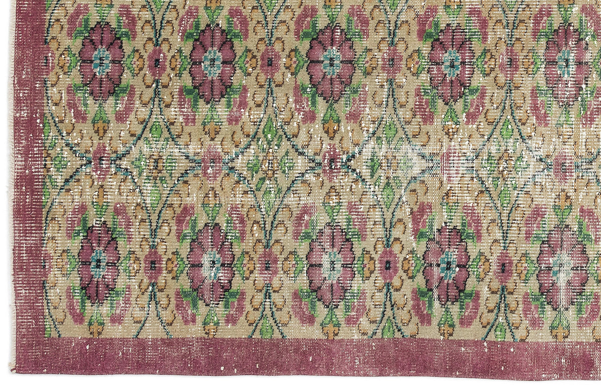 Distressed beige rug with a repeating floral medallion pattern in magenta, green, and teal, featuring a wide solid border.