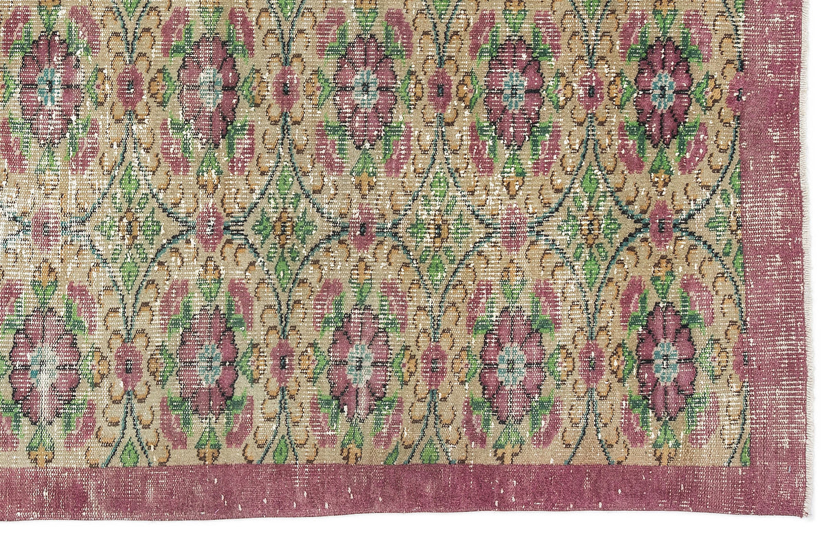 Distressed beige rug with a repeating floral medallion pattern in magenta, green, and teal, featuring a wide magenta border.