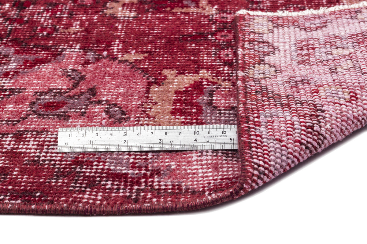 Deep red distressed rug with a floral medallion pattern, shown with a metal ruler for scale on a white background.