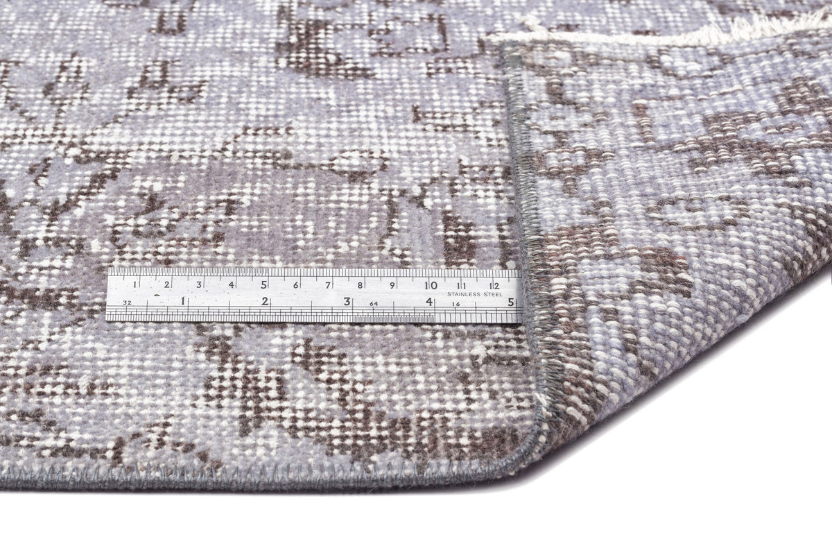 Grey and brown distressed floral pattern rug with a folded corner and a stainless steel ruler for scale.