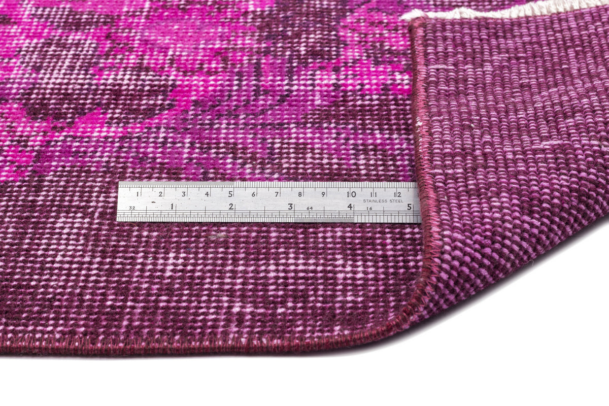 Magenta and deep purple distressed rug with a folded corner and a stainless steel ruler for scale.