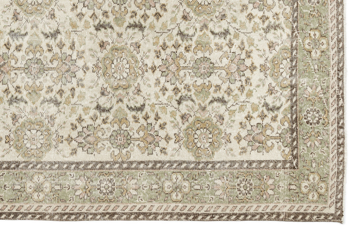 The Nizora - Vintage Floral Rug (6'1 x 10'0) features an ornate, symmetrical floral and geometric design in muted beige, cream, green, and brown tones with a detailed border along the right and bottom edges.