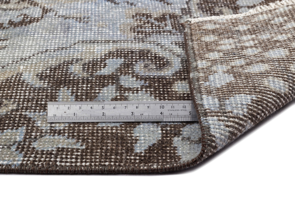 Brown and light blue floral medallion rug with a folded corner and a metal ruler for scale.