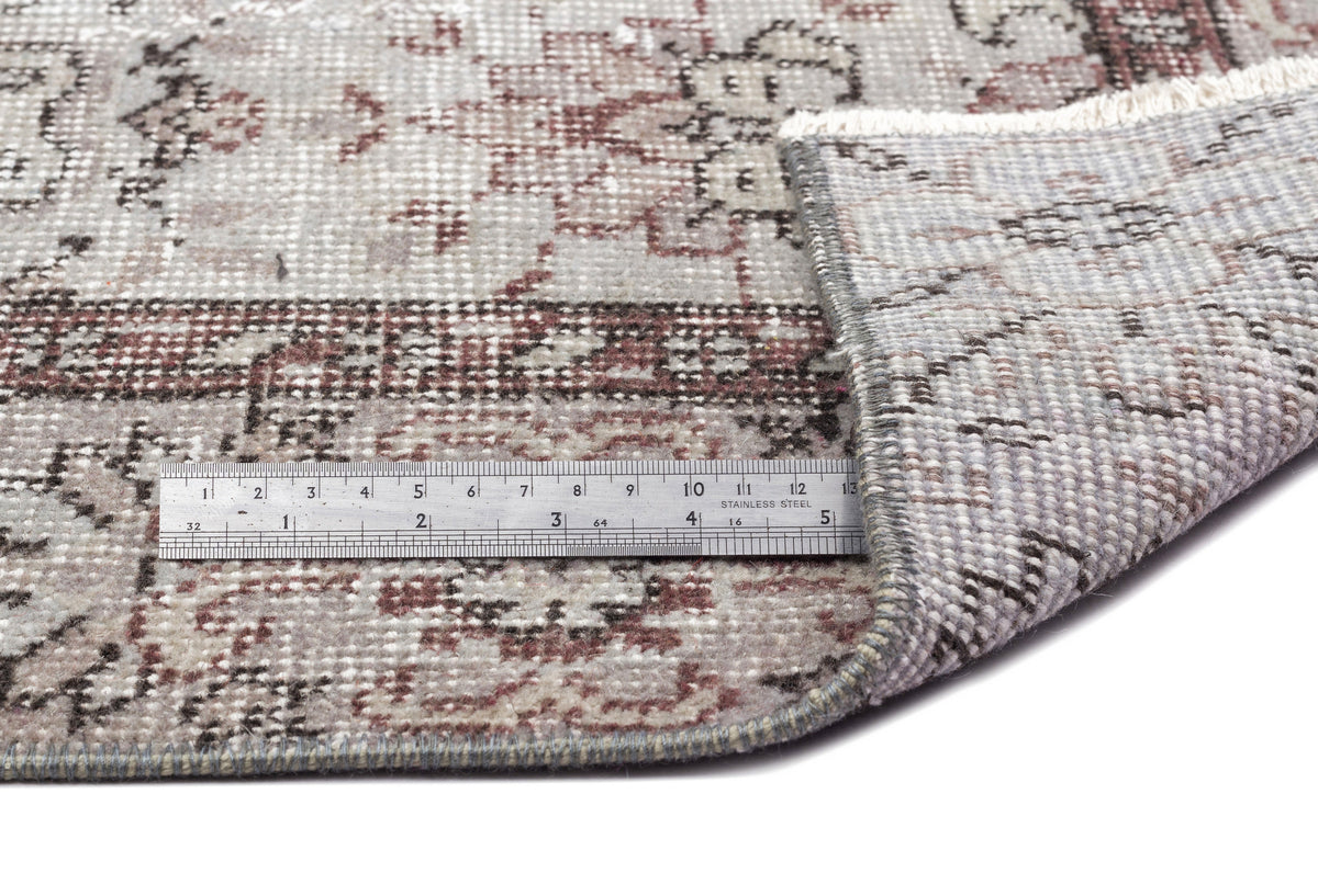 Grey and muted red distressed traditional medallion rug with a metal ruler for scale, isolated on a white background.