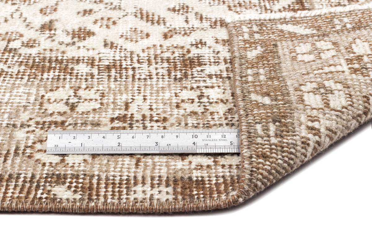 Brown and cream distressed patterned rug with a folded corner and a metal ruler for scale.