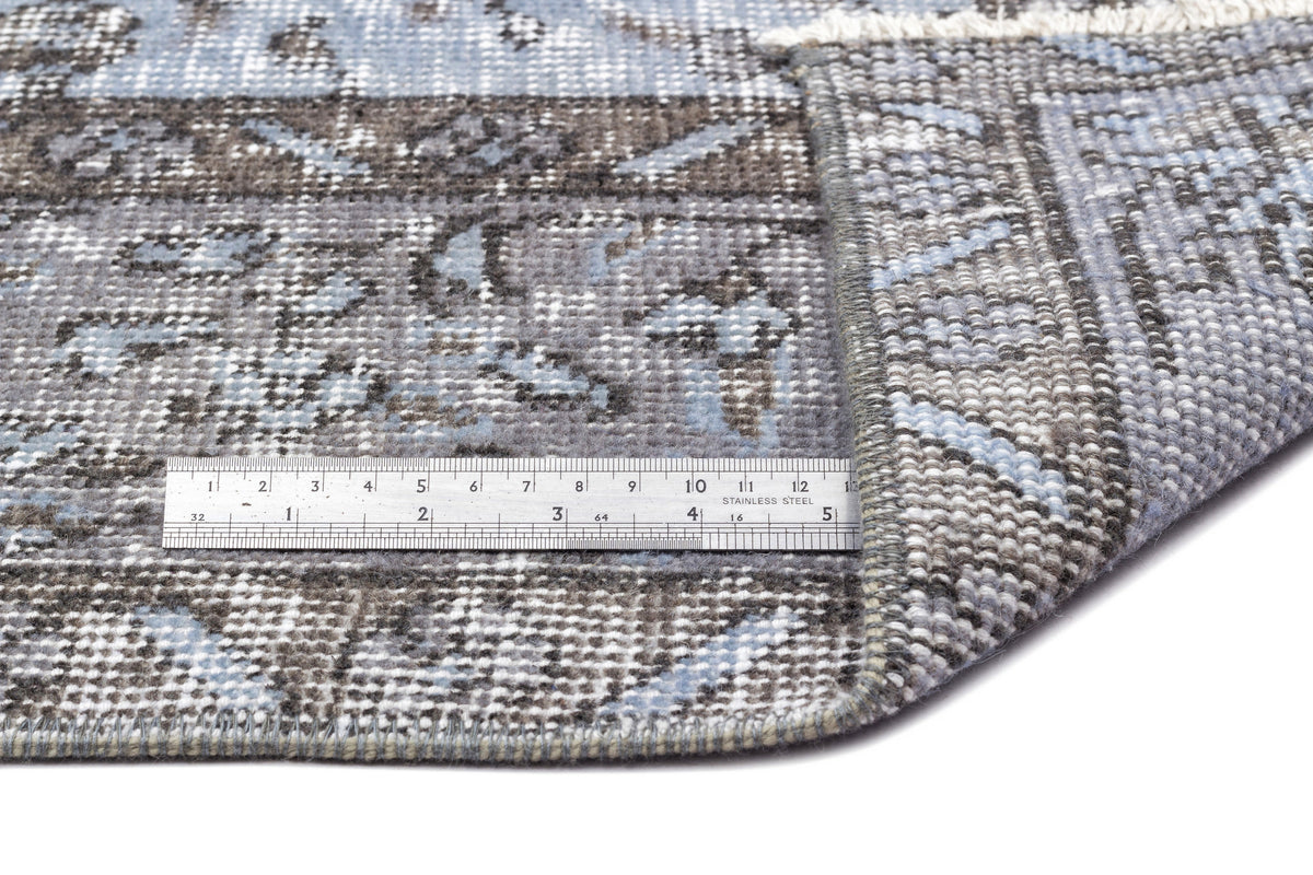 Blue and grey distressed traditional rug with a folded corner and a stainless steel ruler for scale.