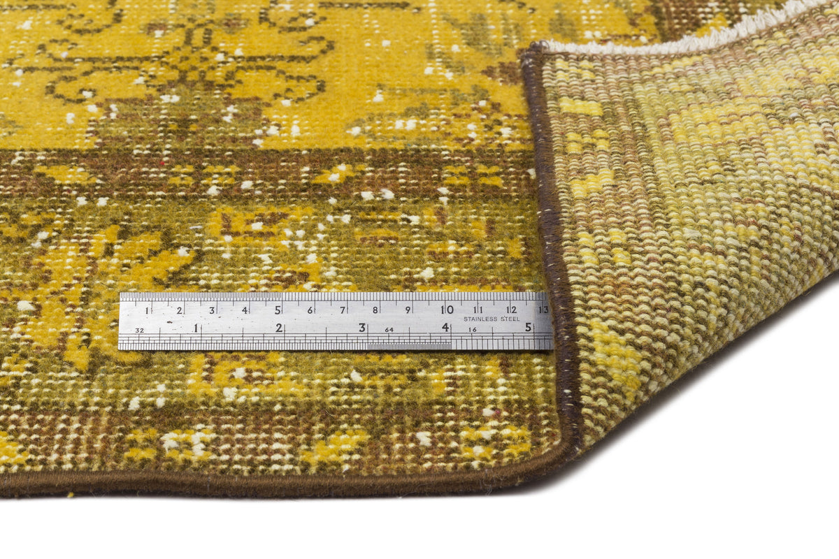Mustard yellow and brown distressed rug with a traditional pattern, showing a metal ruler for scale and a folded corner.