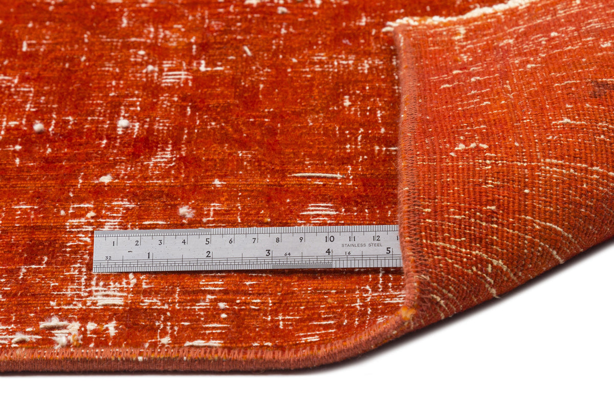 Burnt orange rug with a distressed, worn texture and white flecks, shown with a metal ruler for scale.