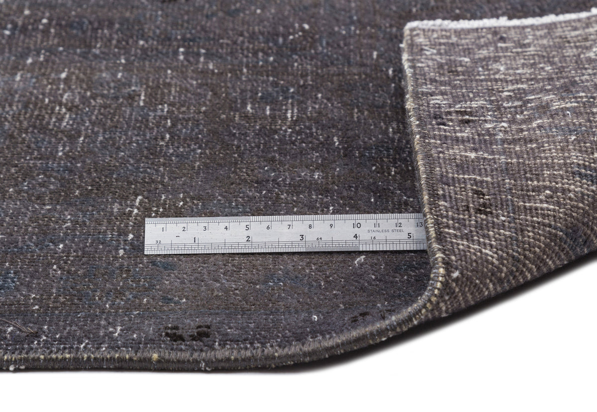 Dark charcoal distressed rug with a folded corner and a stainless steel ruler for scale.