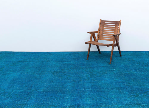 Load image 1 in gallery view. Solid blue distressed-texture rug with a wooden slatted chair, set against a white wall.