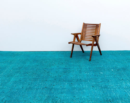 Load image 1 in gallery view. Solid turquoise rug with a distressed, speckled texture, styled with a wooden slatted chair against a white wall.
