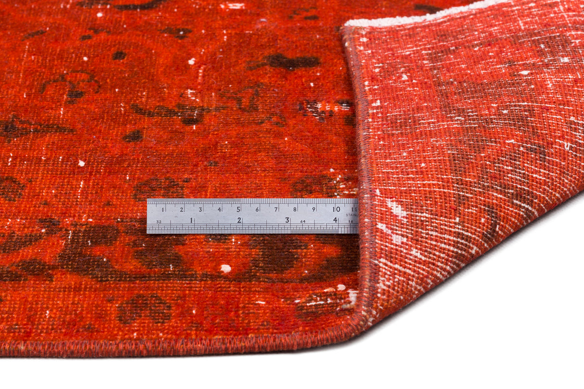 Distressed orange and brown rug with a folded corner and a metal ruler for scale on a white background.