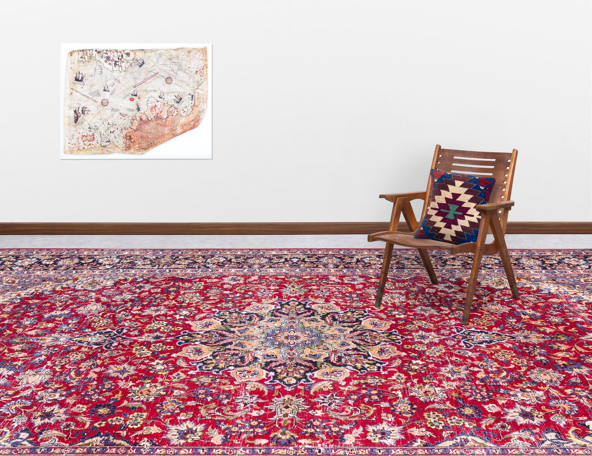 Red traditional Persian-style rug with a central floral medallion, styled in a room with a wooden chair and wall map.