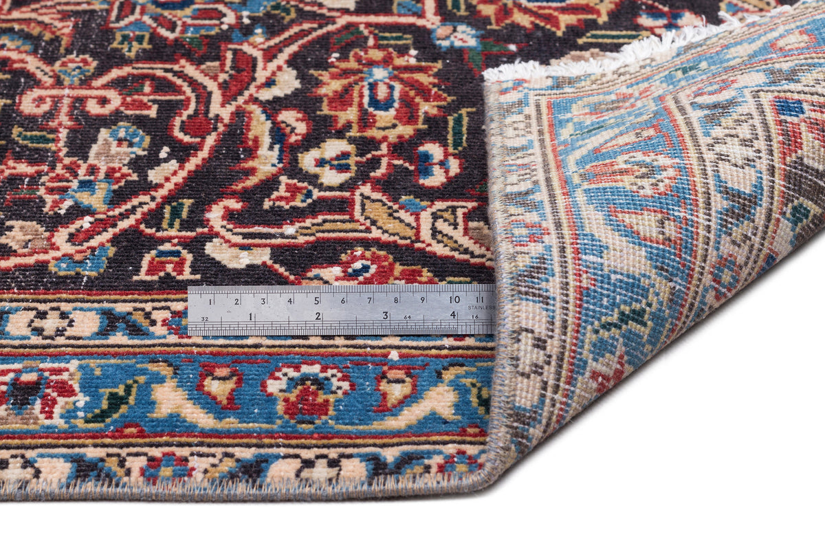 Black, red, and blue traditional Persian-style rug with floral motifs, shown with a metal ruler for scale.