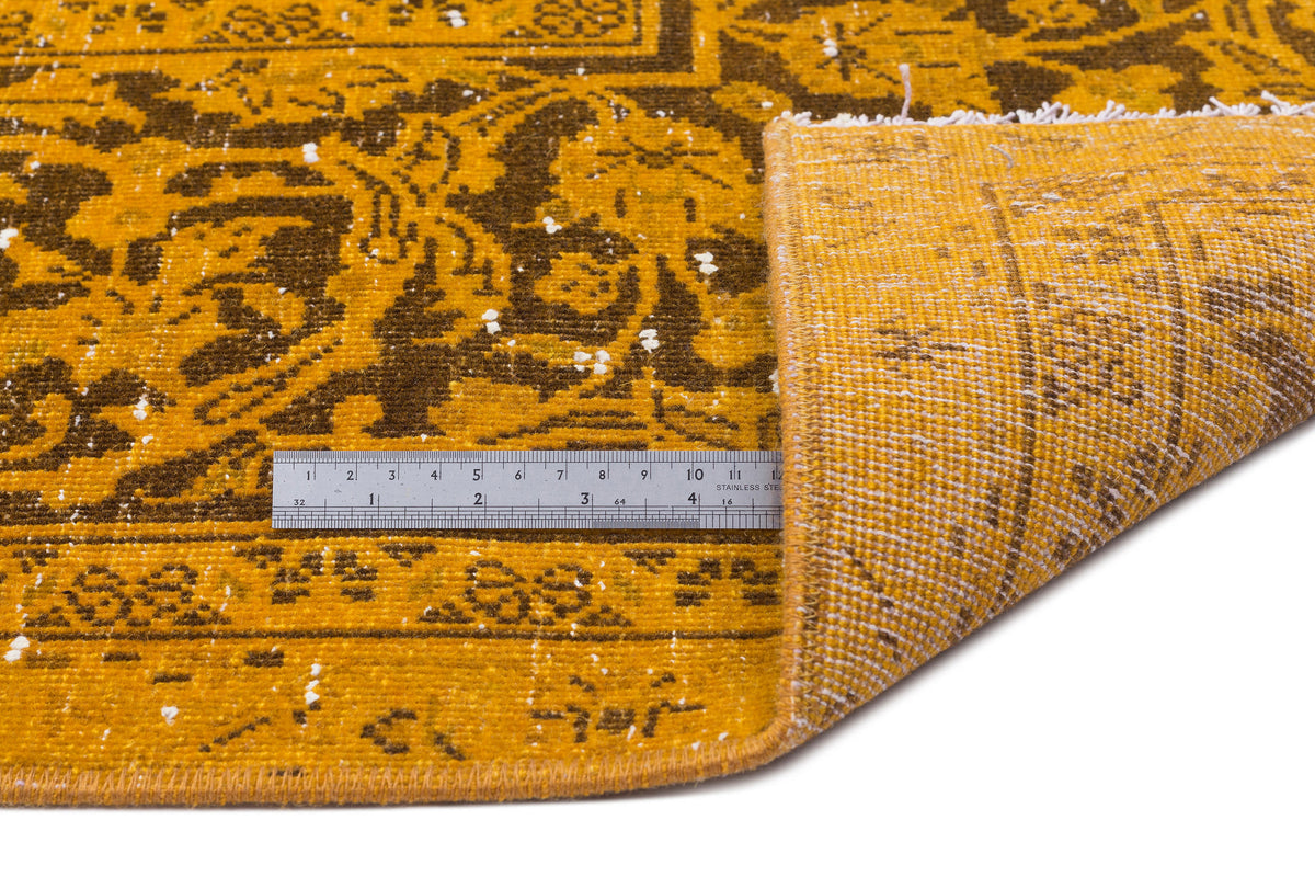 Mustard yellow and dark brown distressed rug with a traditional floral medallion pattern and a metal ruler for scale.