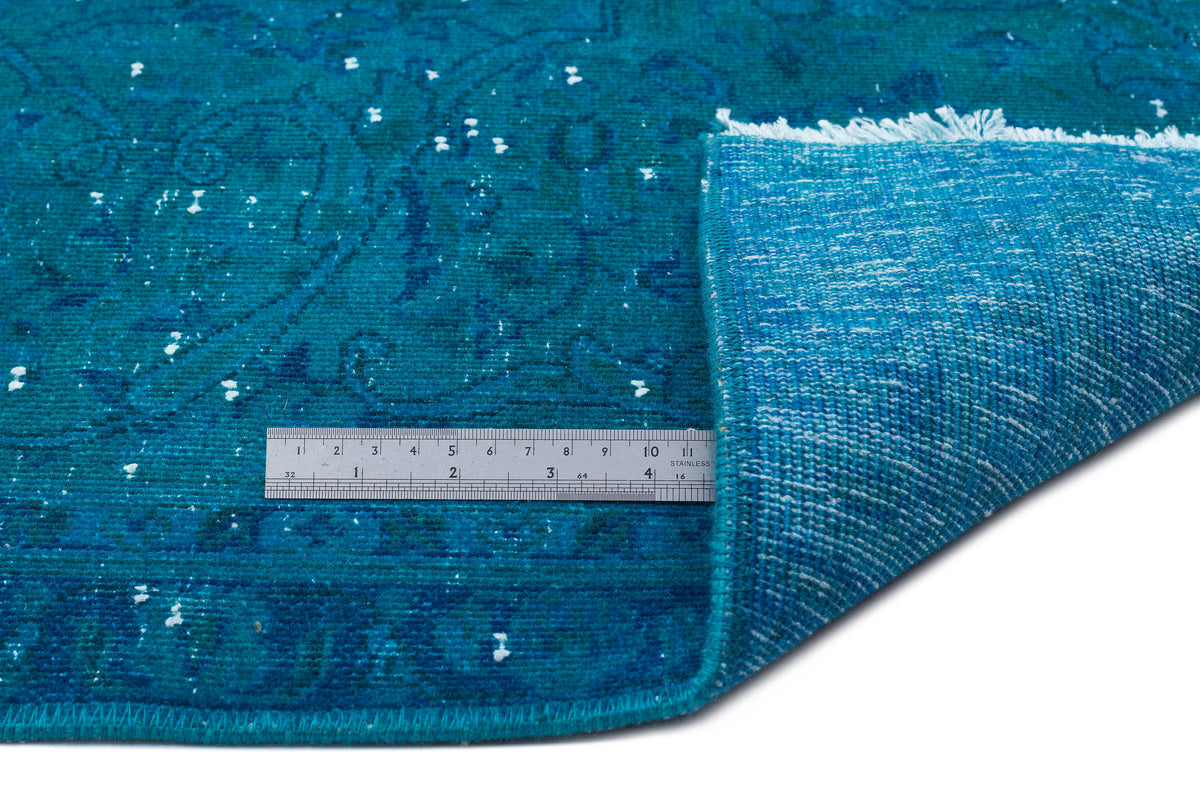 Teal distressed medallion rug with white flecks and a folded corner showing the backing, measured by a metal ruler.
