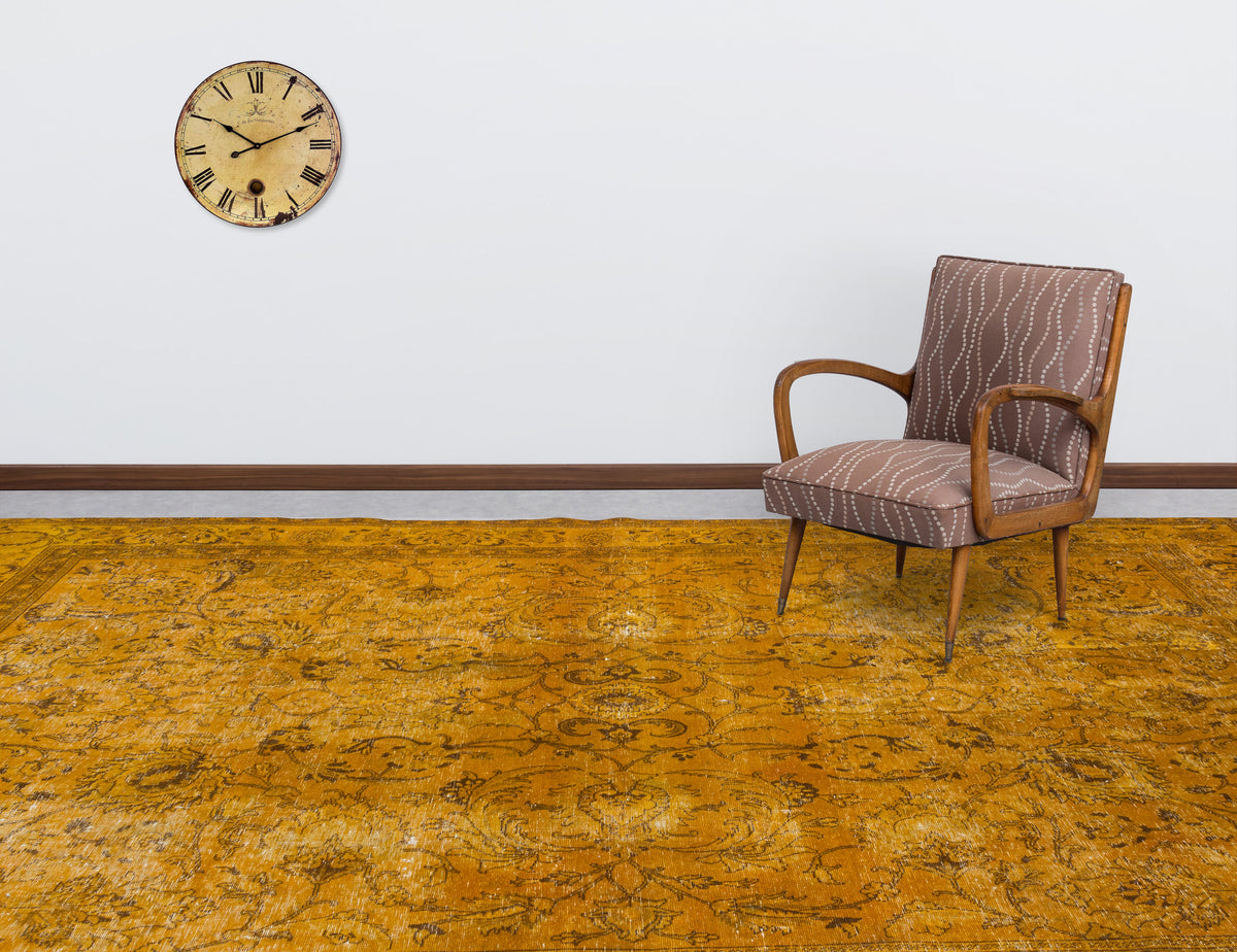 Distressed mustard yellow rug with a traditional floral pattern, styled in a room with a vintage chair and wall clock.