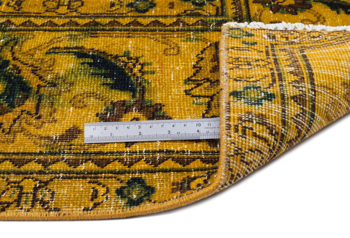 Mustard yellow rug with a distressed floral pattern, green and brown accents, and a white fringe, shown with a ruler.