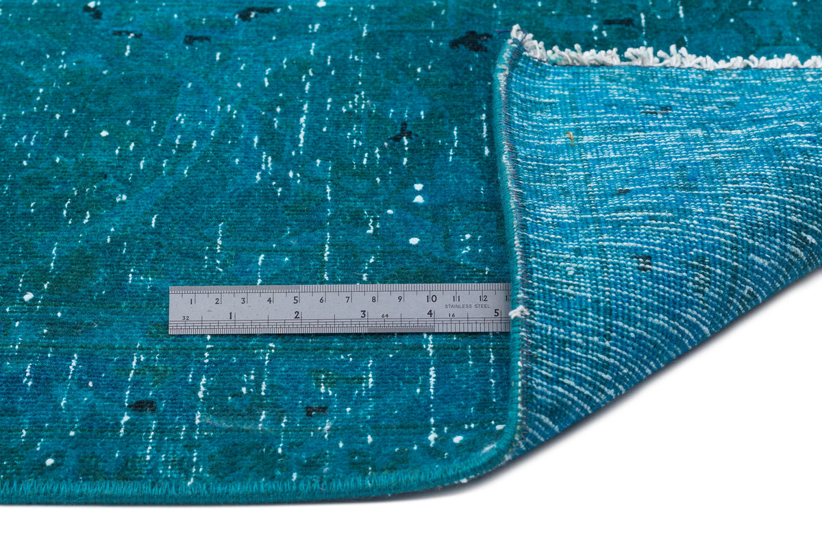 Teal distressed rug with white speckled pattern and white fringe, shown with a metal ruler for scale on a white background.