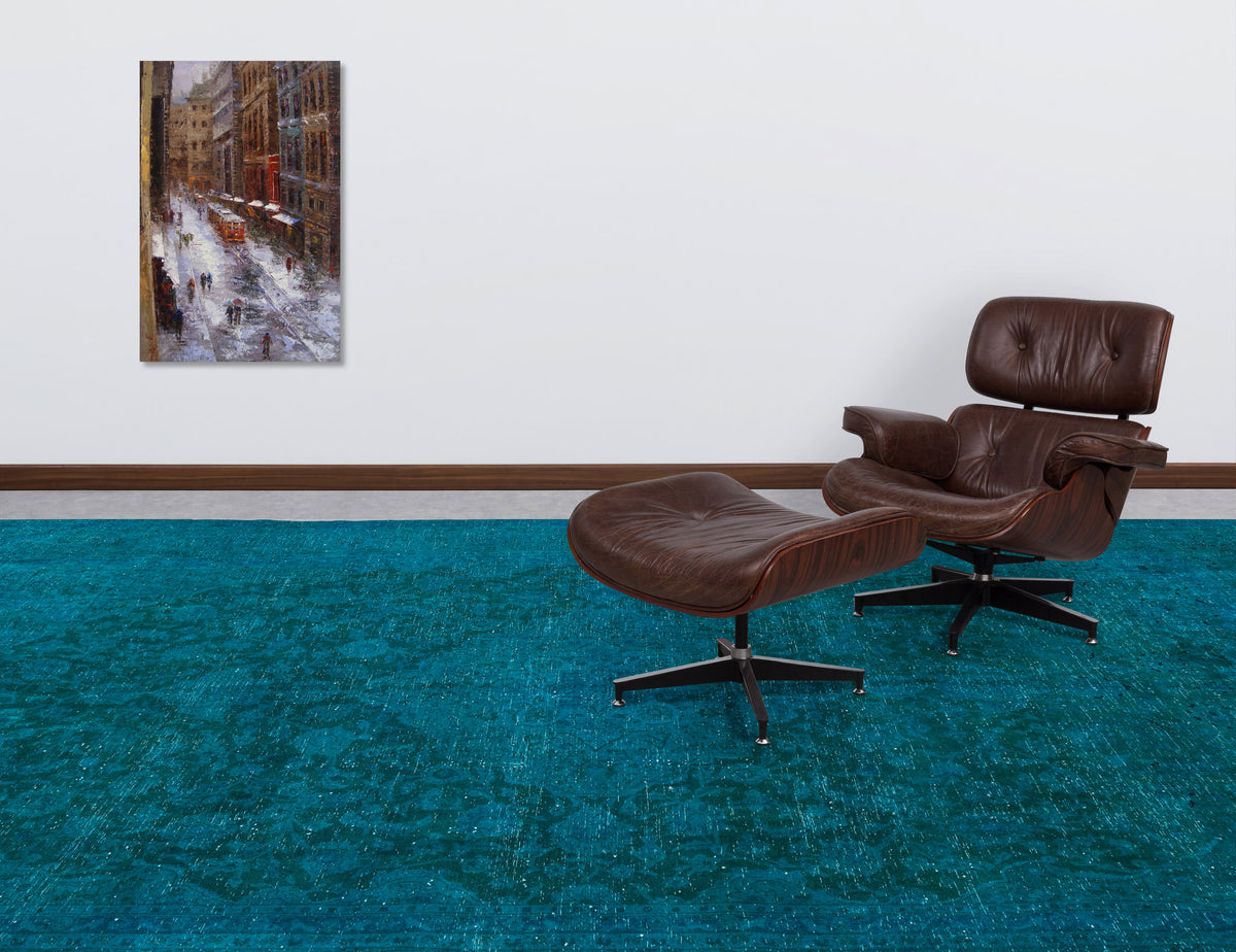 Teal distressed-pattern rug in a room with a brown leather lounge chair and a city street painting on the wall.