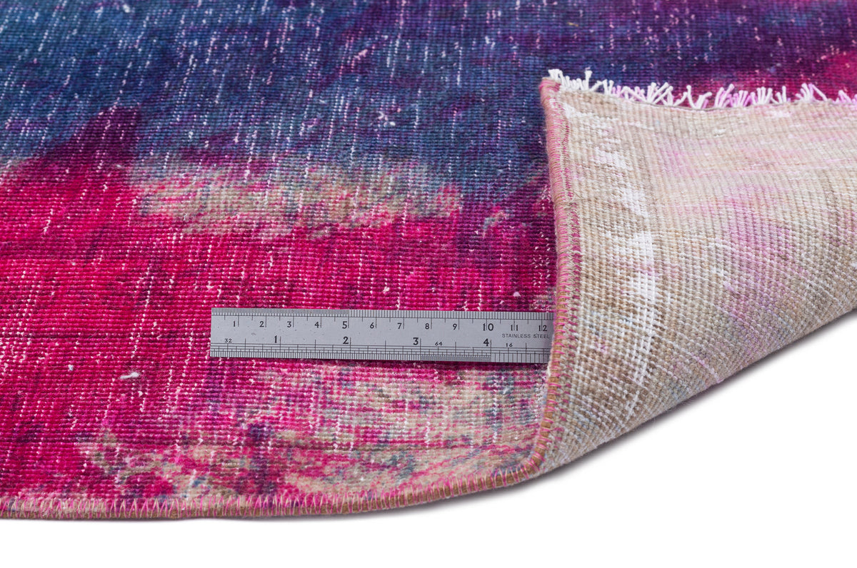 Magenta and navy blue distressed abstract rug with a folded corner revealing a beige backing and a metal ruler.