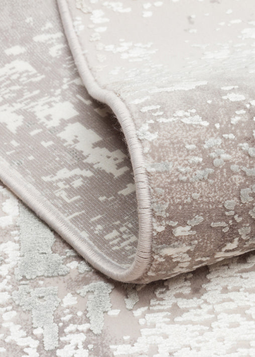Taupe and white rug with a distressed, abstract mottled pattern, shown in a close-up folded corner view.