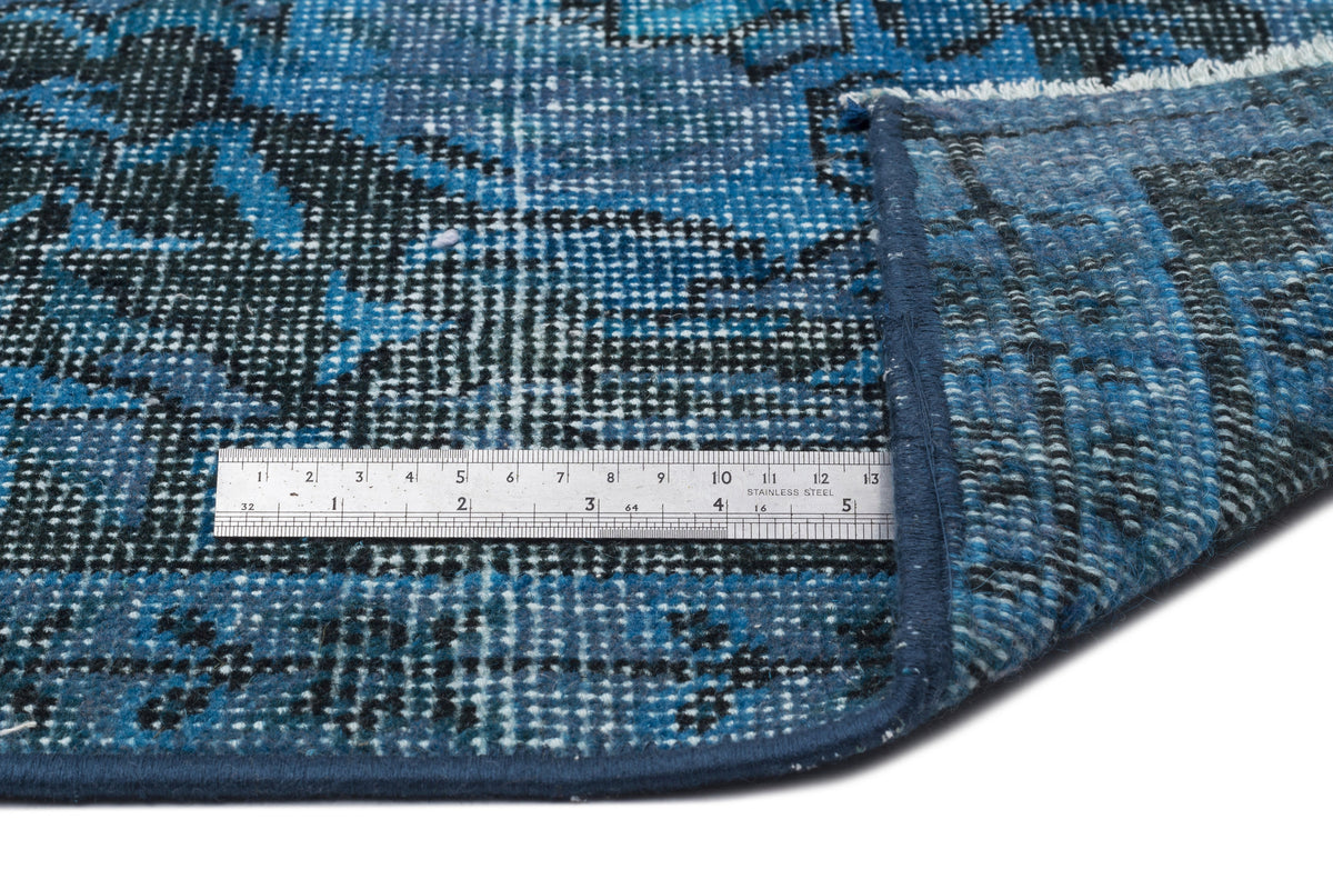Blue and black distressed medallion rug with a folded corner and a stainless steel ruler for scale.