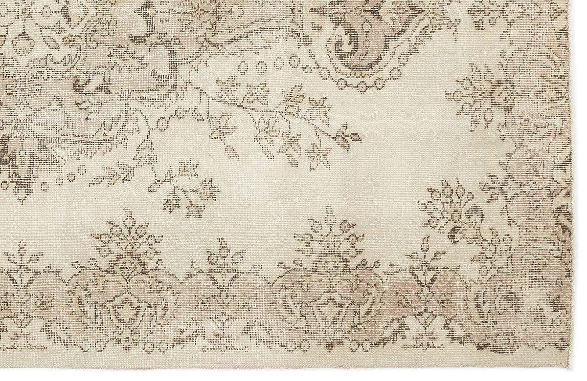 Cream and beige rug with a distressed, faded floral medallion pattern.
