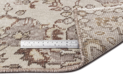 Load image 1 in gallery view. A close-up of the Luboane - Vintage Medallion Rug (6'1 X 9'1), with one corner folded to show the underside. A metal ruler measures its thickness and intricate patterns. The rug displays neutral beige and brown tones.