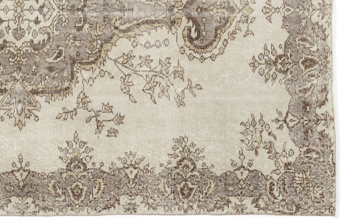 A section of the Luboane Vintage Medallion Rug (6'1 x 9'1) displays a faded beige and brown floral vine design with a decorative border, featuring intricate, slightly distressed patterns for an authentic vintage overdyed look.