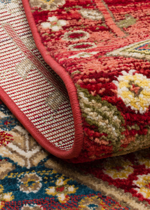 Load image 1 in gallery view. Red, blue, and yellow traditional floral rug with a folded corner showing the textured pile and bound edge.