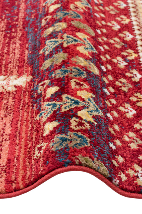Load image 1 in gallery view. Red rug with a folded corner featuring a traditional tribal pattern in blue, gold, and cream accents.