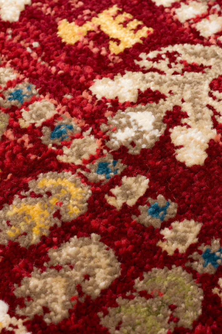 Deep red rug with a textured pile featuring traditional floral motifs in cream, yellow, and blue accents.
